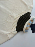 White knit sweater with embossed logo detail and black ribbed collar edge