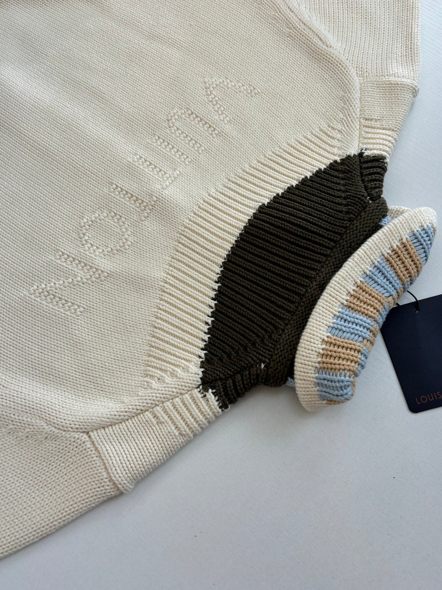 White knit sweater with embossed logo detail and black ribbed collar edge