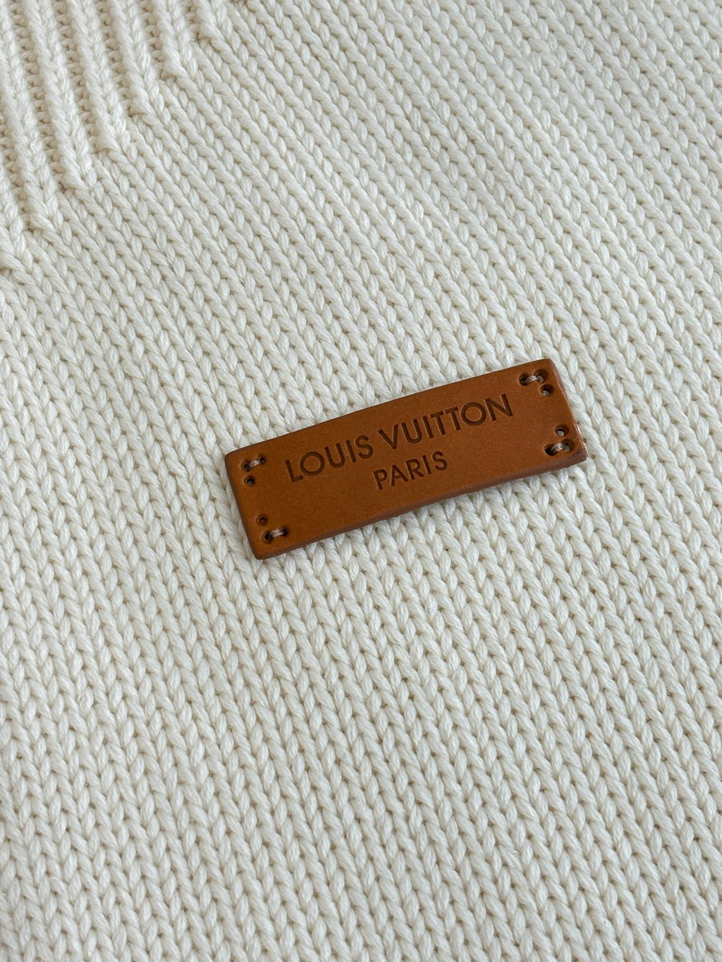 Louis Vuitton leather label on white knit fabric reading “LOUIS VUITTON PARIS”