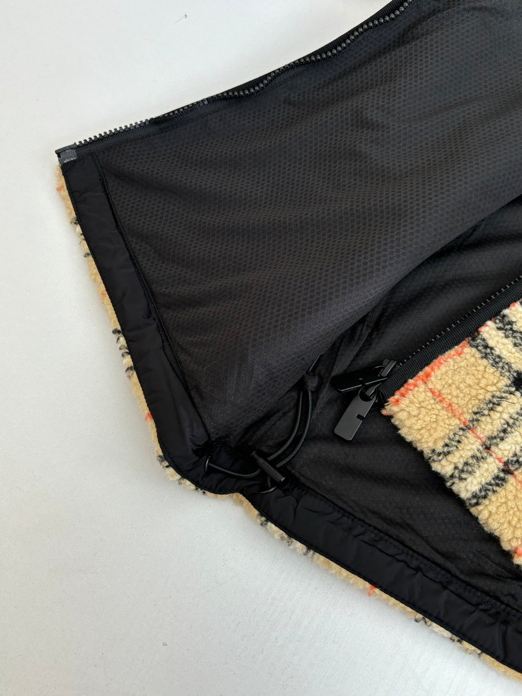 Black mesh lining panel and black drawcord along plaid jacket edge