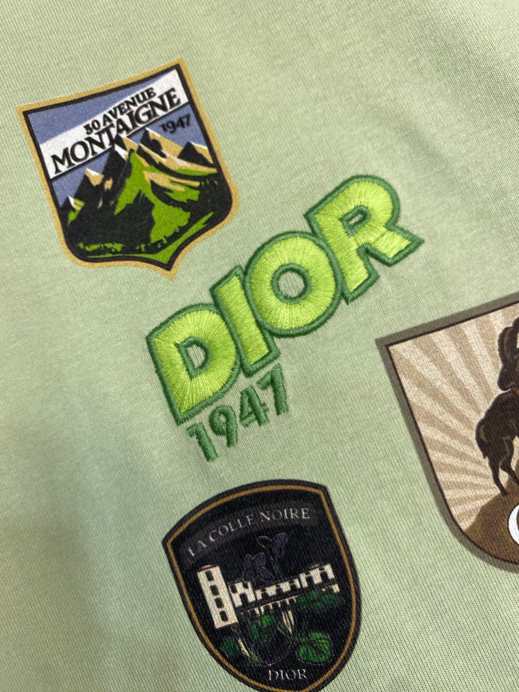 Close-up of light green Dior logo T-shirt with “Dior 1947” and crest graphic