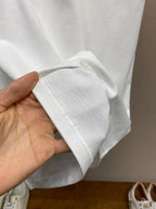 White Christian Dior T-shirt sleeve cuff and hem detail, hand holding