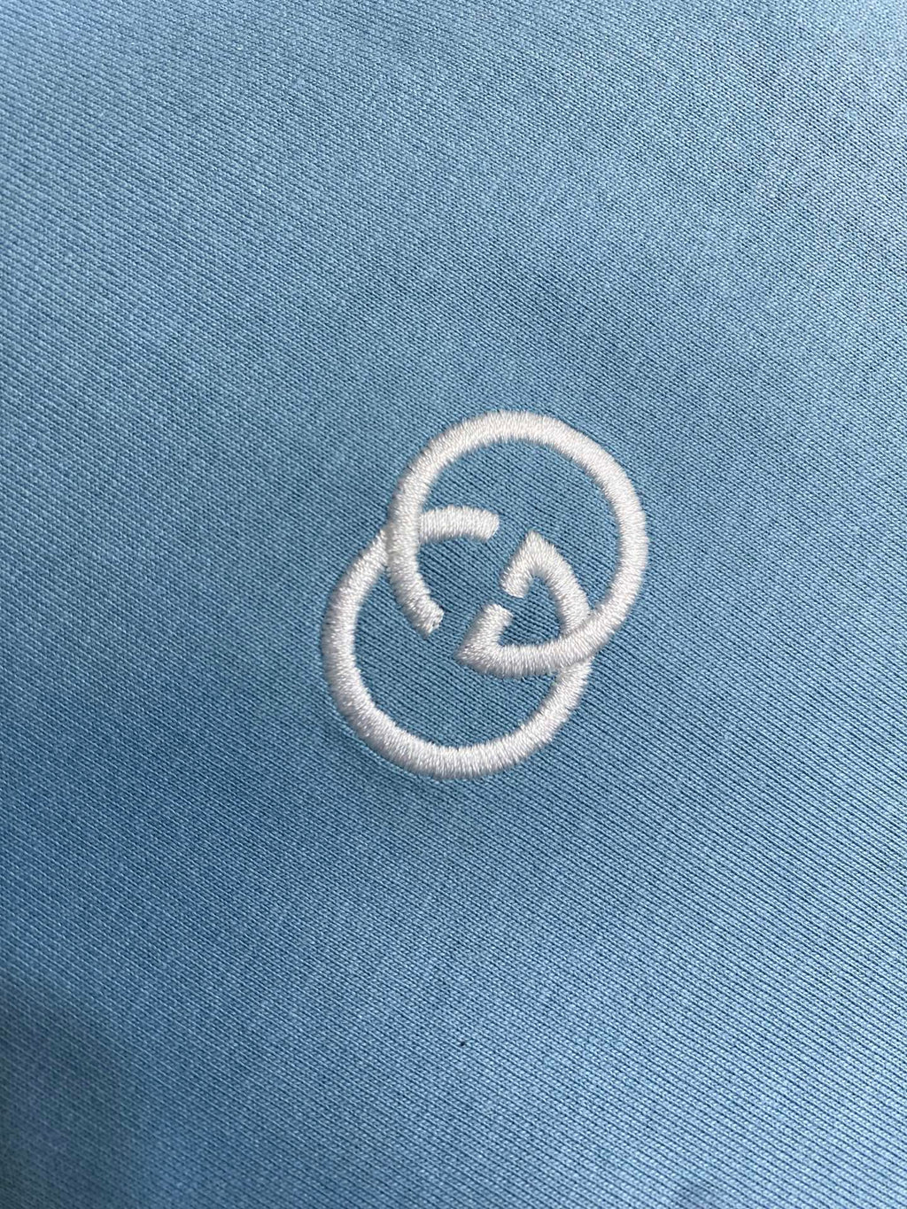 Embroidered white Gucci logo on light blue fabric