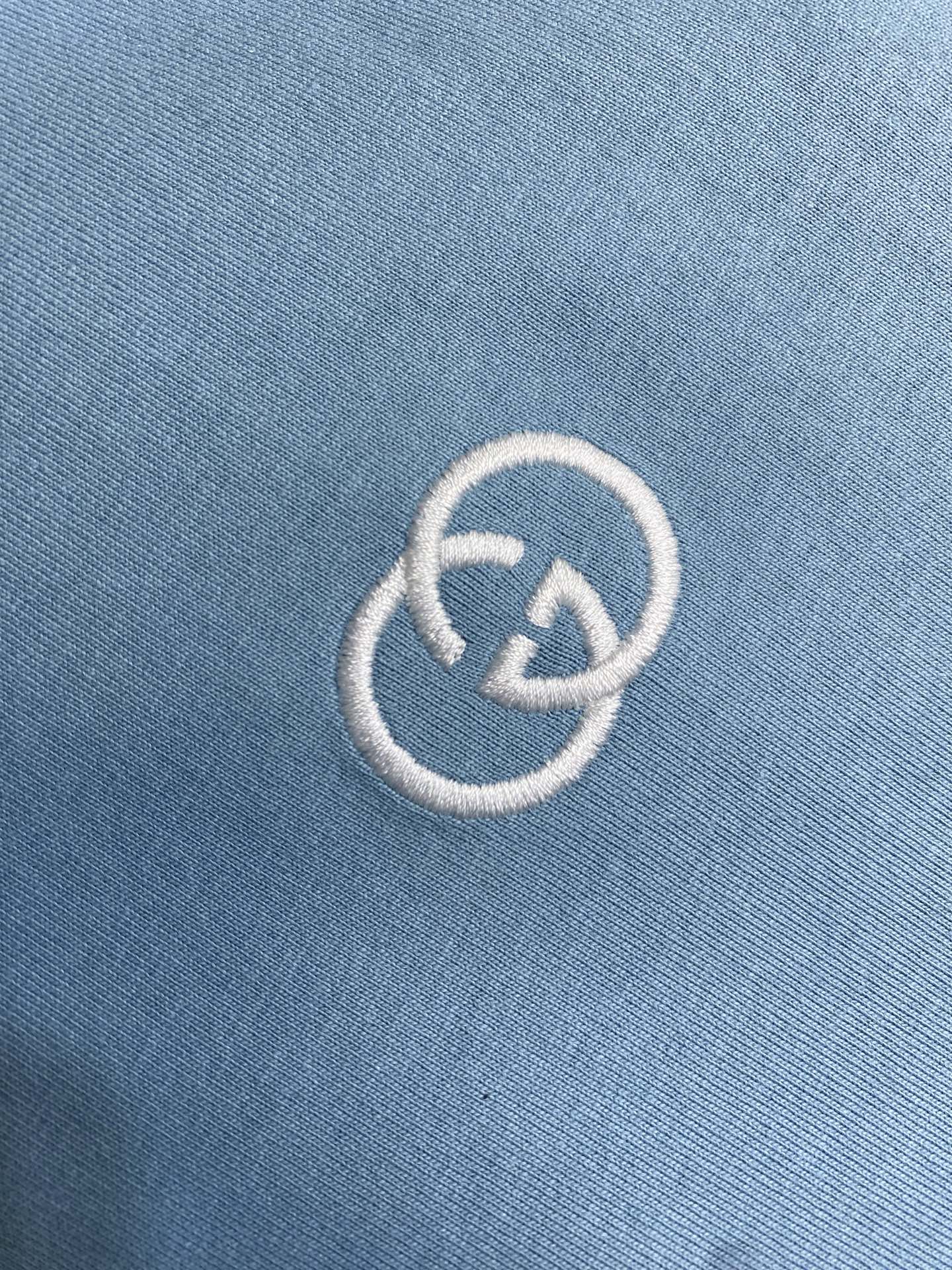 Embroidered white Gucci logo on light blue fabric