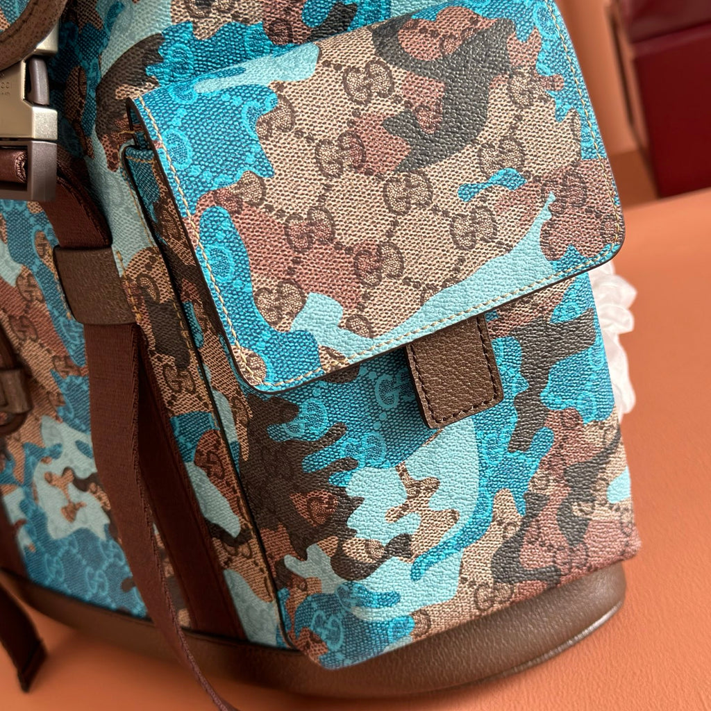 Gucci camo-print backpack front corner with flap, buckle strap, and brown leather bottom