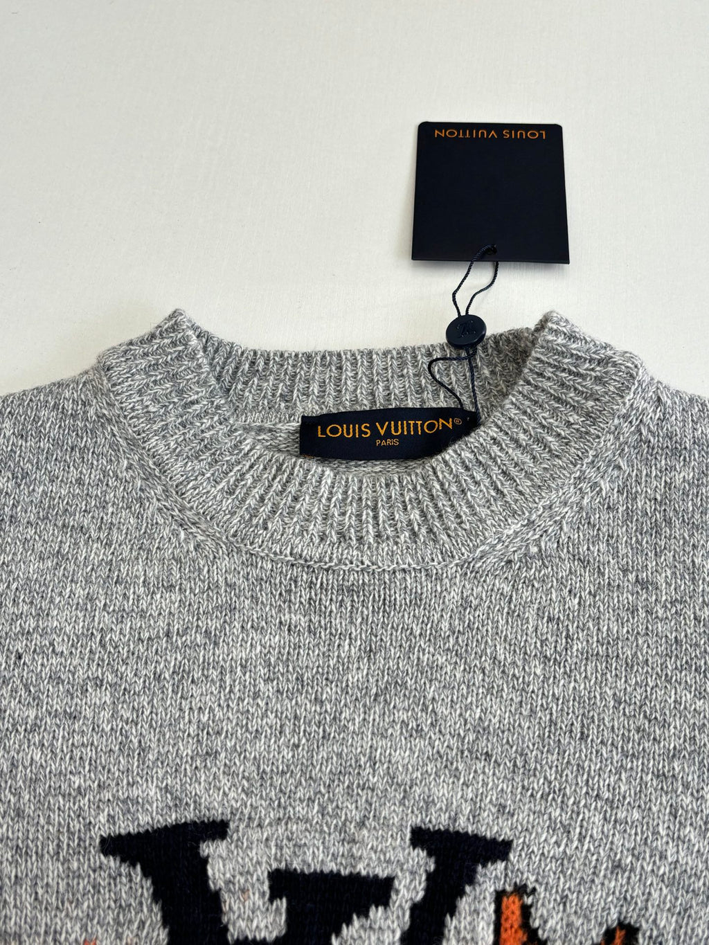 Gray knit sweater neckline with ribbed collar and hang tag labeled Louis Vuitton