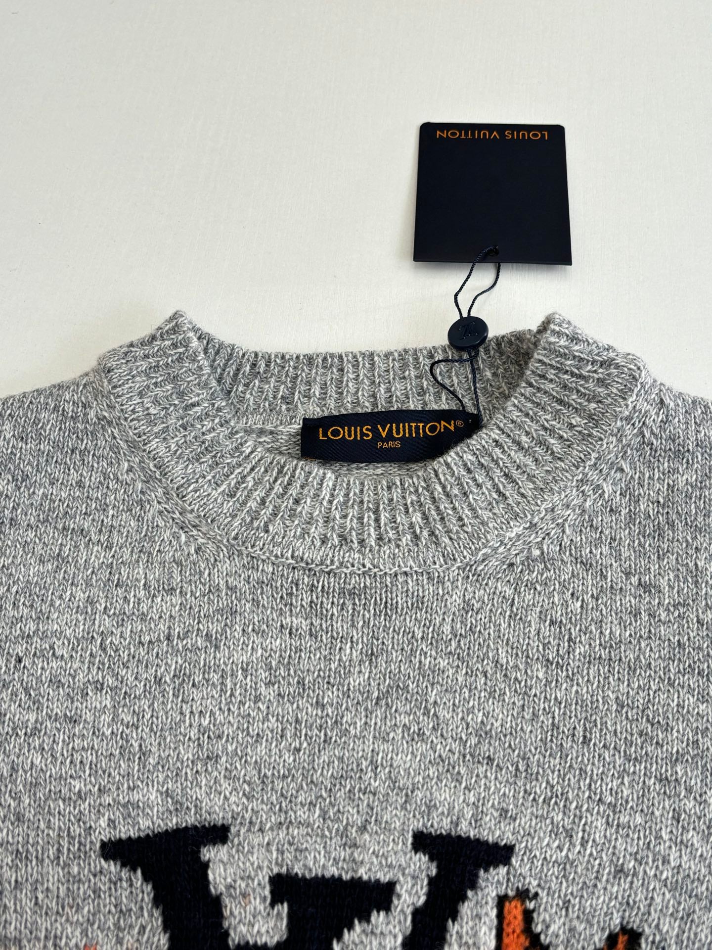 Gray knit sweater neckline with ribbed collar and hang tag labeled Louis Vuitton