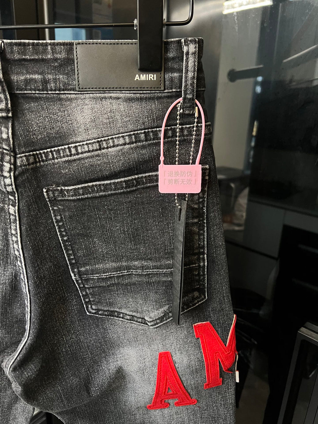 Gray denim jeans with front pocket, pink hang tag, and red 'AM' lettering