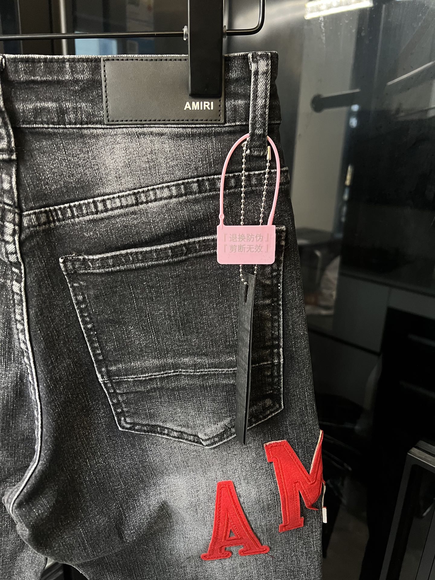 Gray denim jeans with front pocket, pink hang tag, and red 'AM' lettering