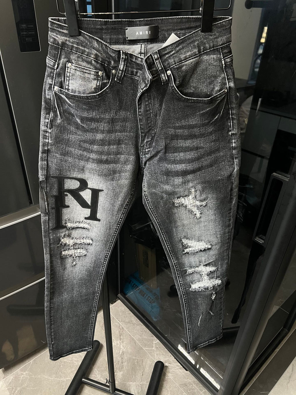 Distressed light-gray denim jeans with knee rips and large black R applique