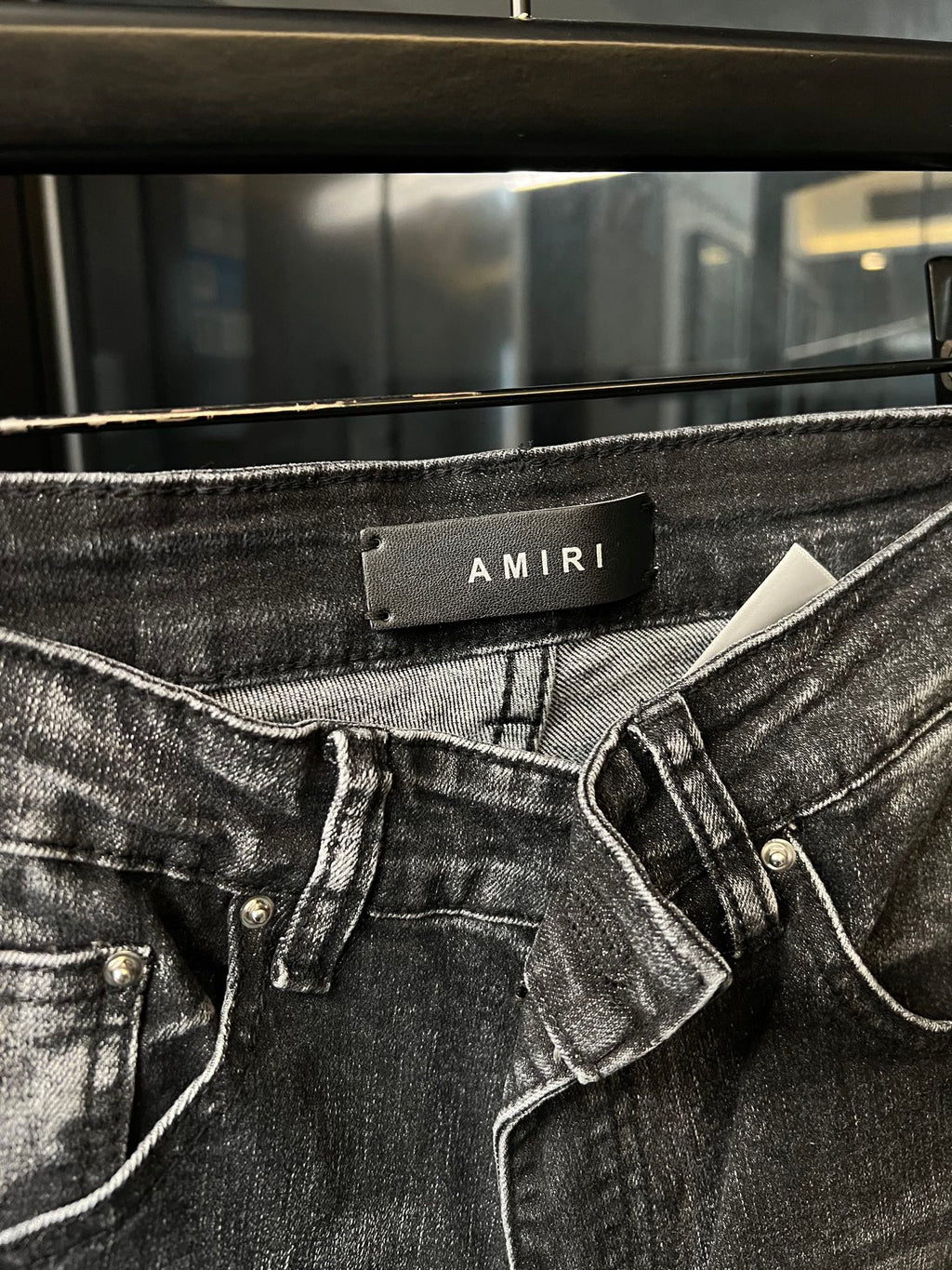 Light-gray denim jeans waistband close-up with AMIRI label and belt loops