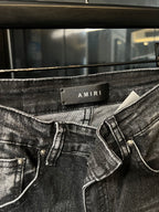 Light-gray denim jeans waistband close-up with AMIRI label and belt loops