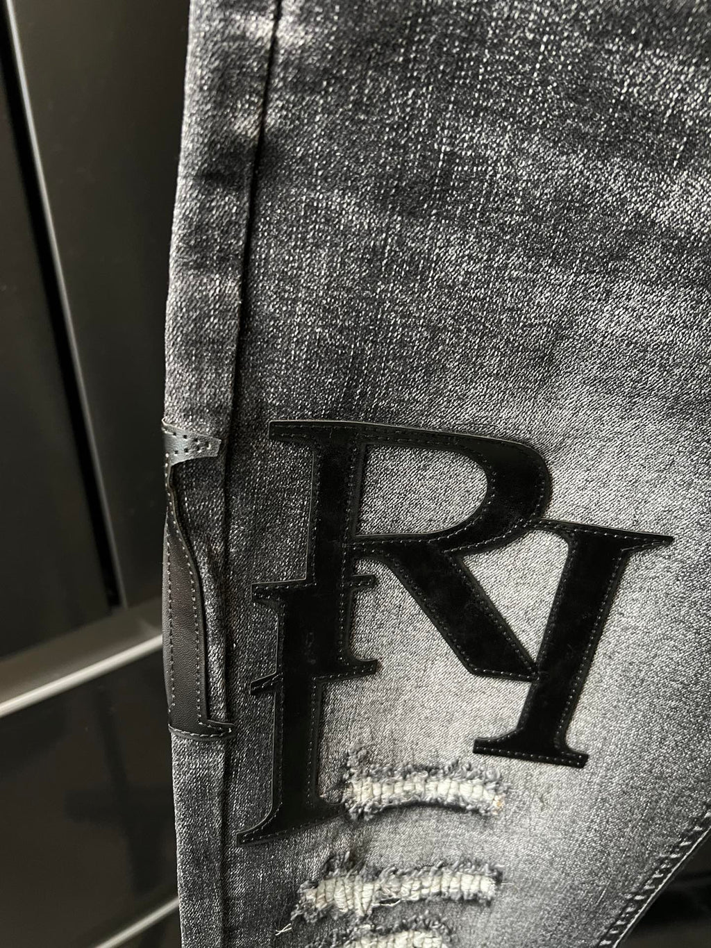 Light-gray denim jeans detail with large black R applique on the leg