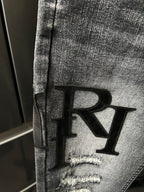 Light-gray denim jeans detail with large black R applique on the leg