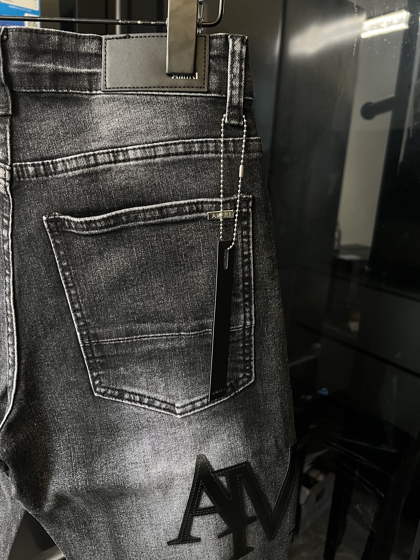 Light-gray denim jeans close-up with front pocket and AM logo print