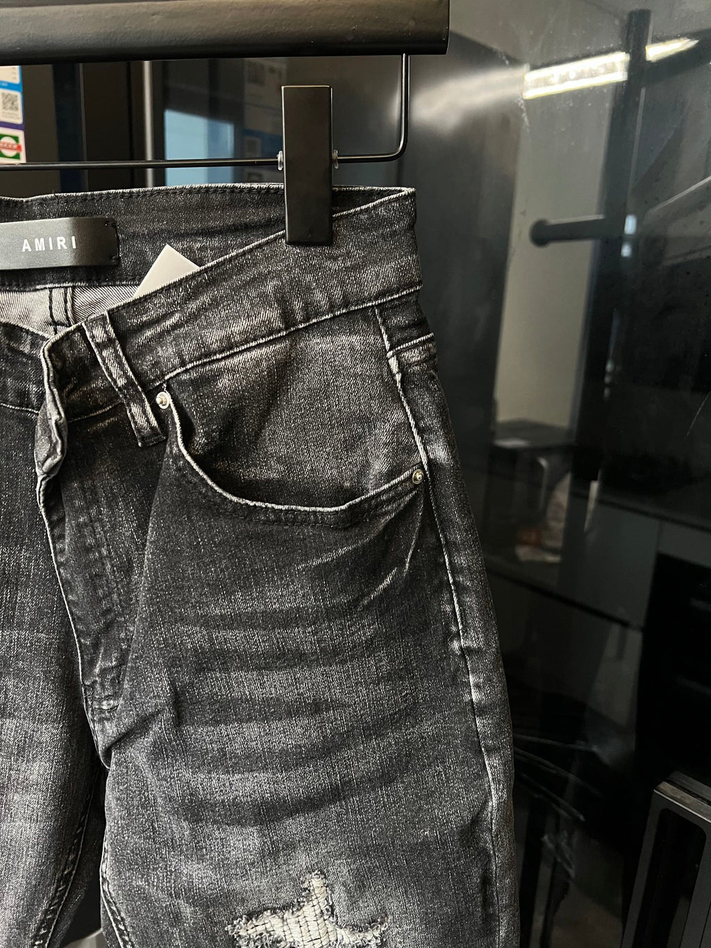 Light-gray denim jeans close-up with curved pocket seams and small knee rip