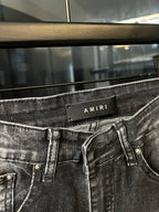 AMIRI waistband label on light-wash denim jeans with button fly and front belt loops
