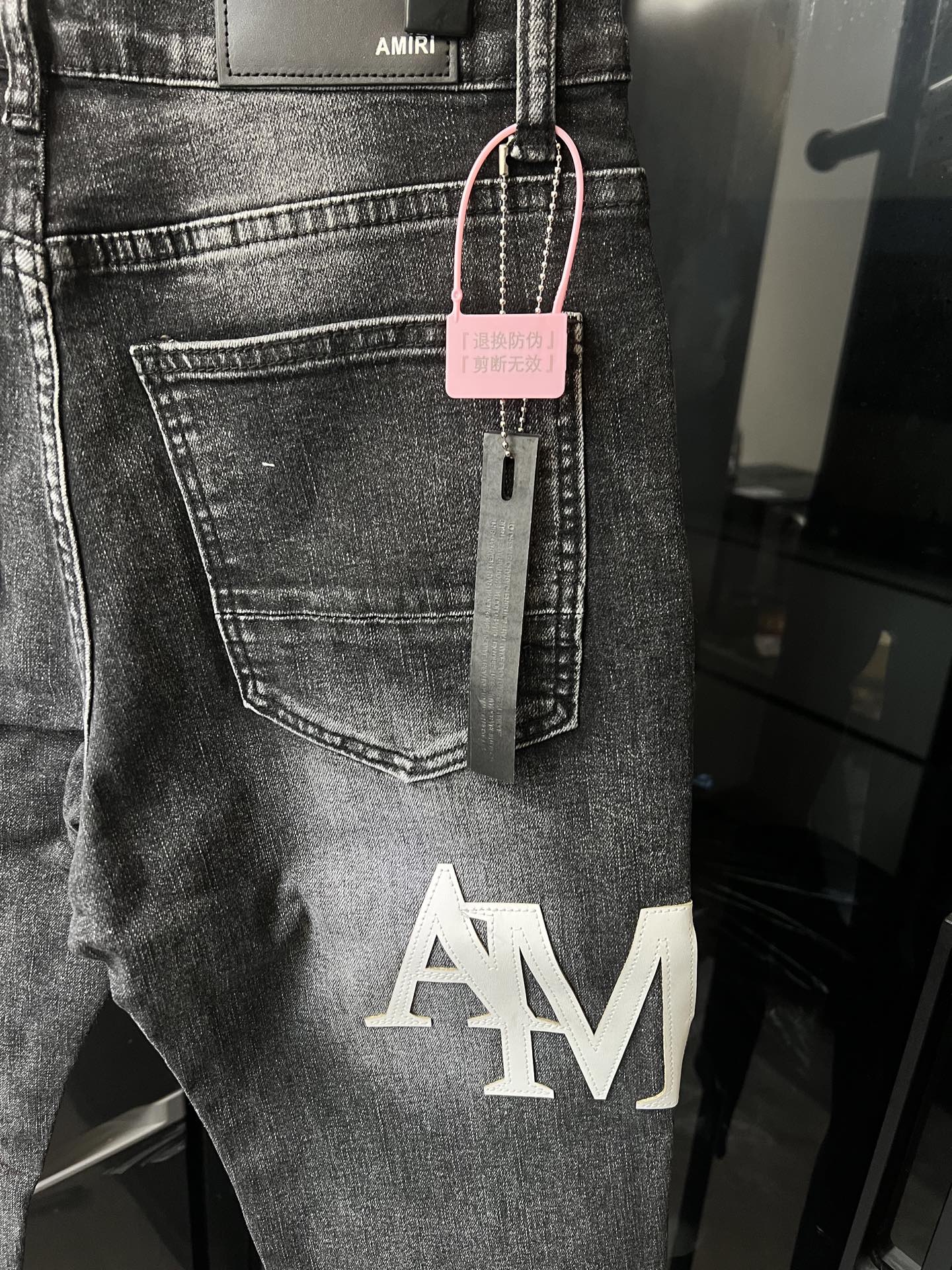 Light-wash denim jeans with AM logo print and pink tag hanging at waistband