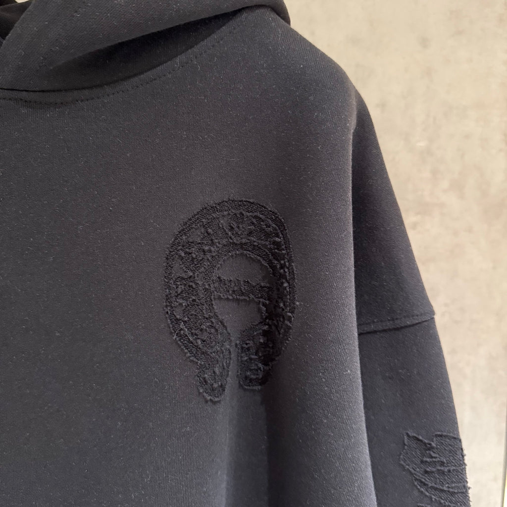 Black hoodie close-up with oval face applique and distressed sleeve graphic