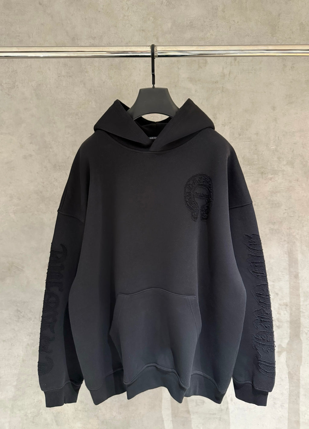 Black long-sleeve pullover hoodie with hood and front pocket, subtle logo patch