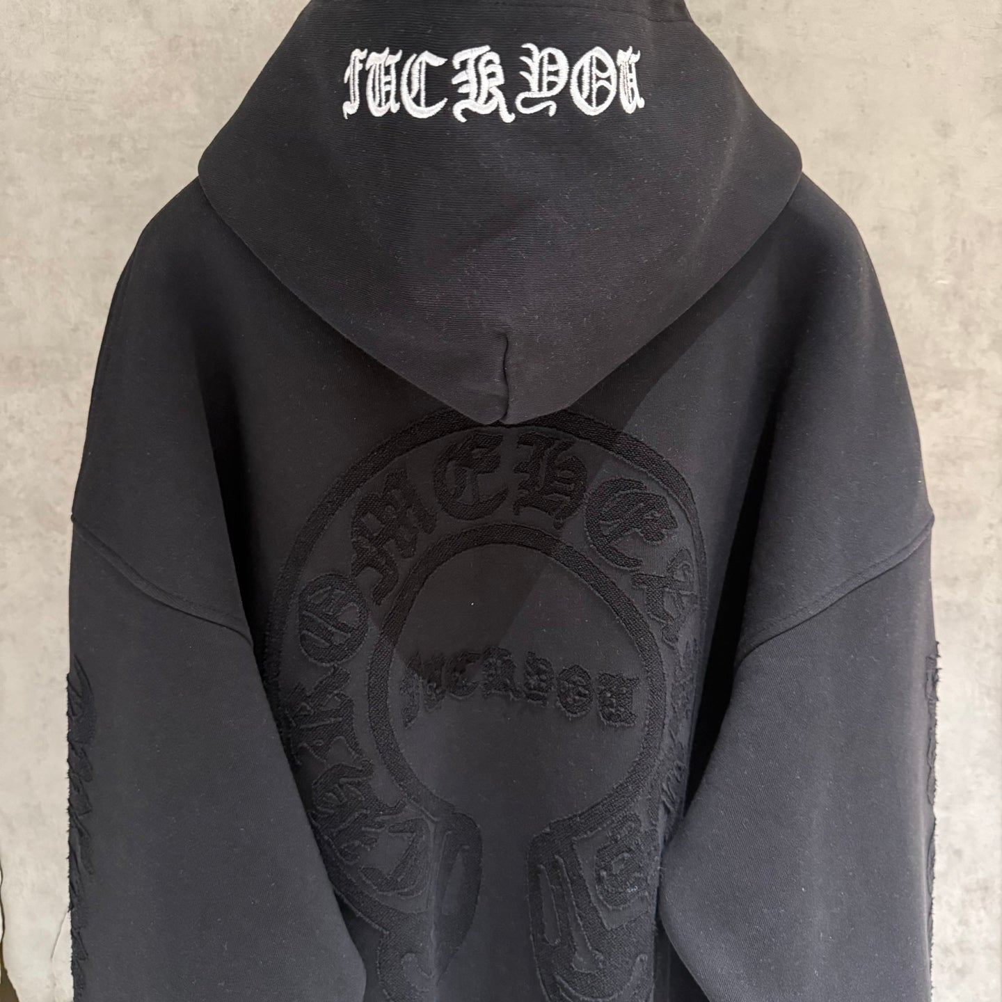 Black hoodie back with hood and white stylized text, featuring a large oval logo