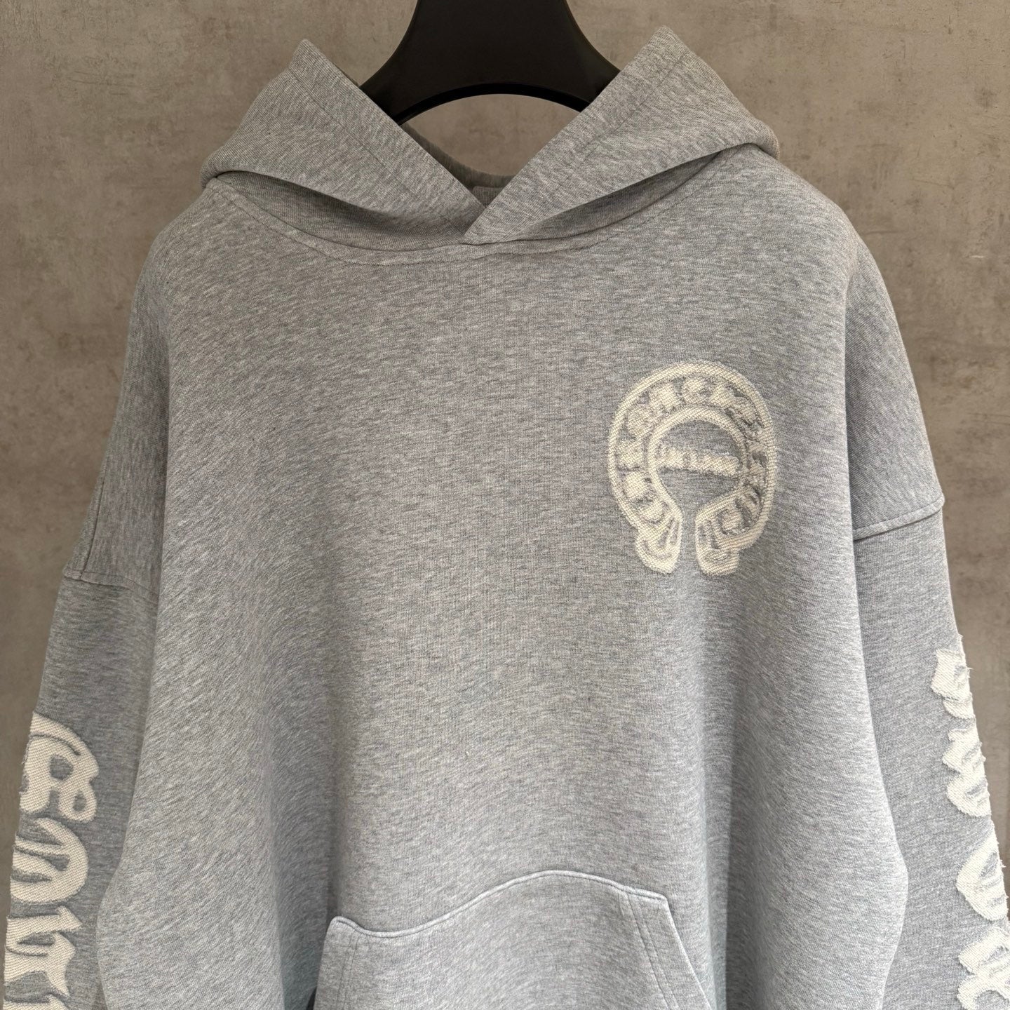 Gray hoodie with hood and small chest emblem, front view.