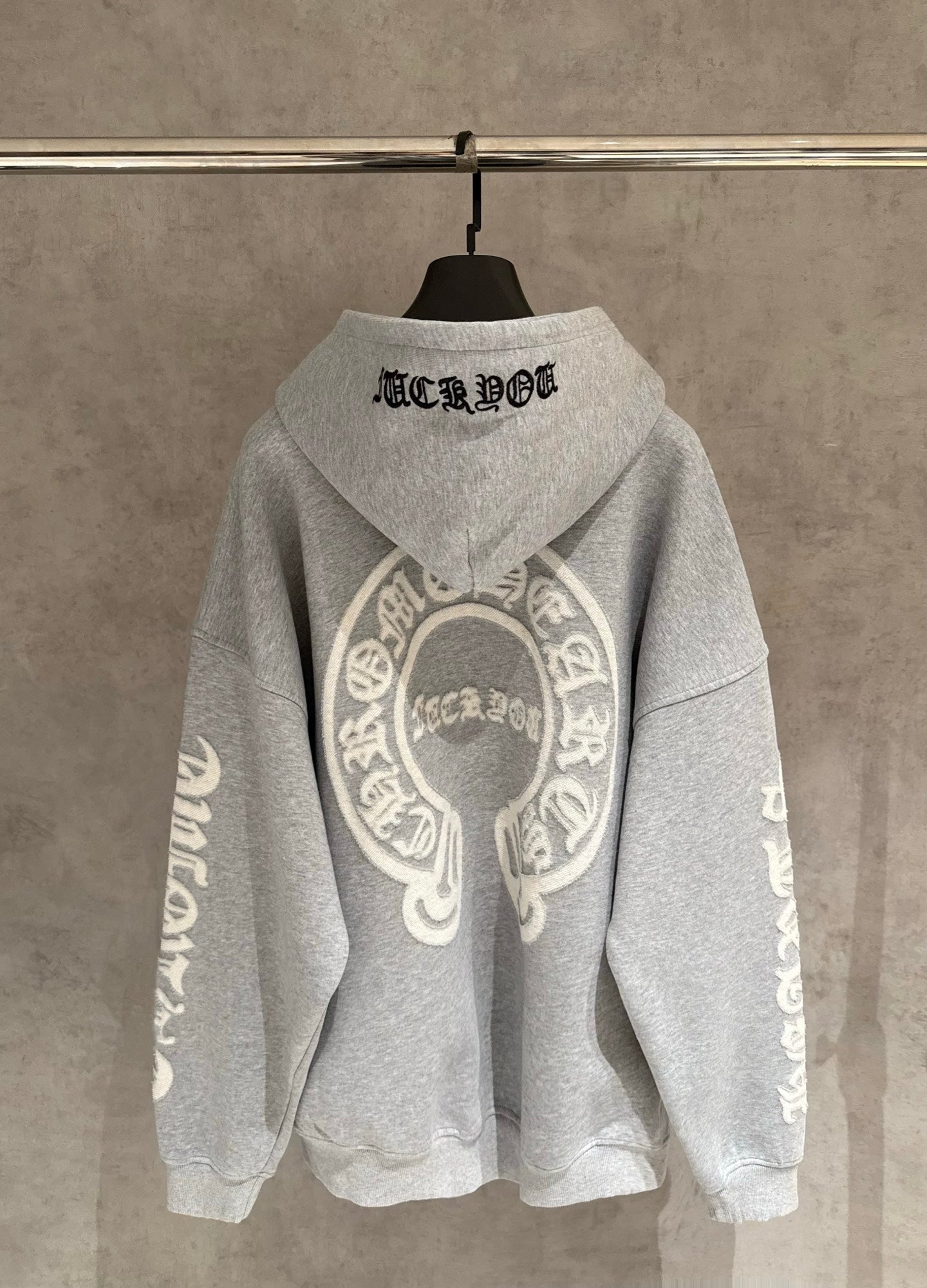 Gray hoodie back view with large circular emblem and black hood word graphic.