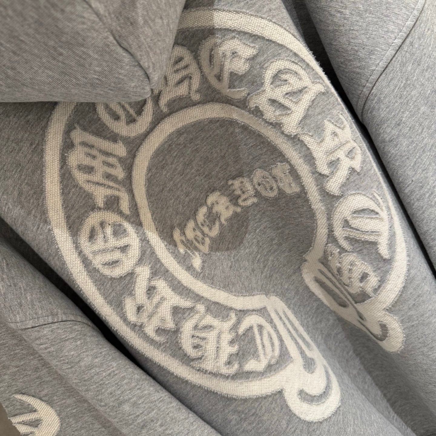 Gray hoodie back with oversized circular emblem graphic.