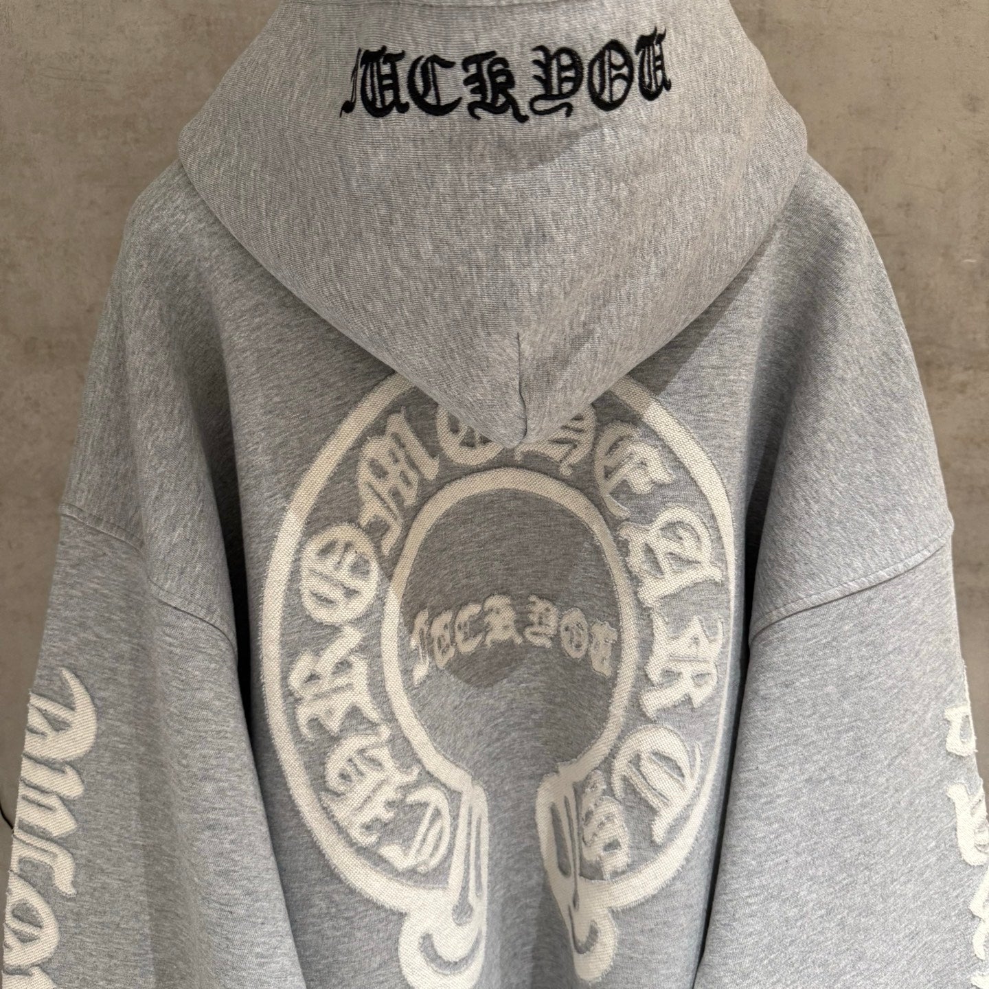 Gray hoodie back view with black word text and large circular emblem.