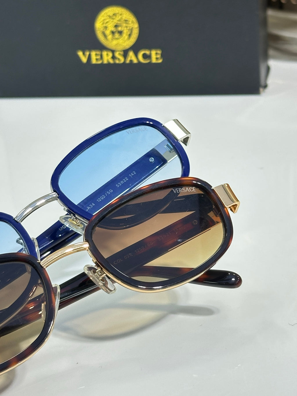 Versace sunglasses close-up with blue temple and dark lenses, gold hardware