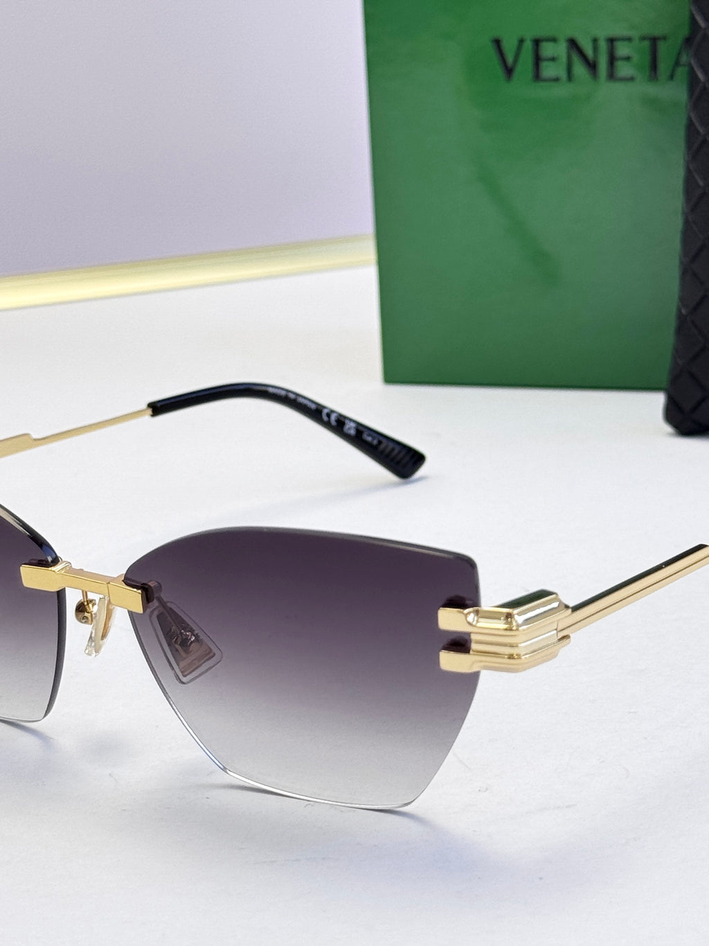 Bottega Veneta sunglasses, close-up of black temple and gold arms with dark tinted lenses