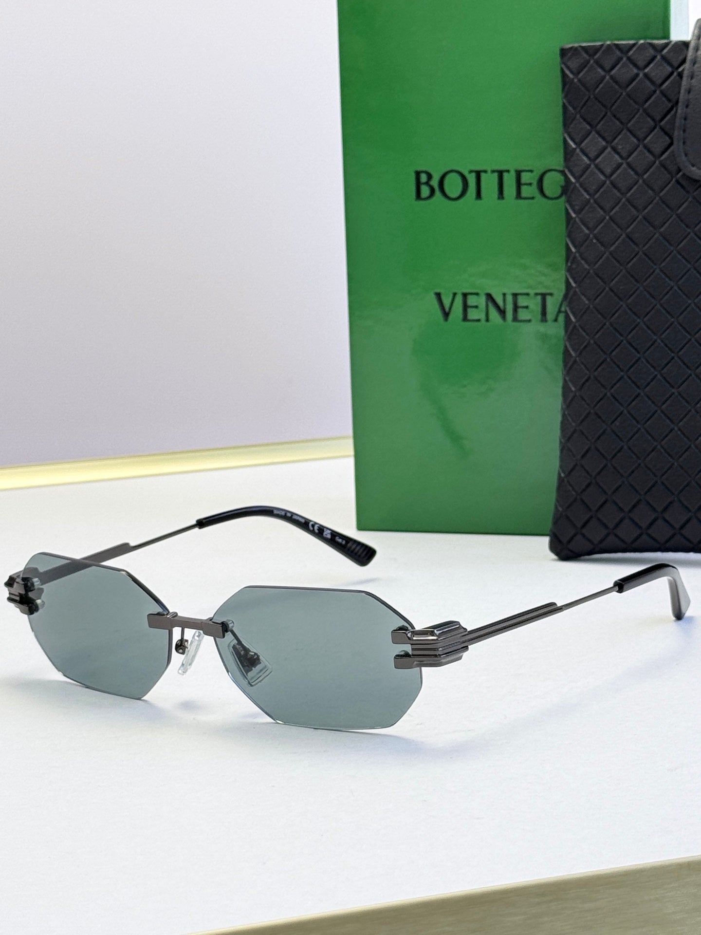 Bottega Veneta sunglasses with black frame and light gray tinted lenses, octagonal shape.