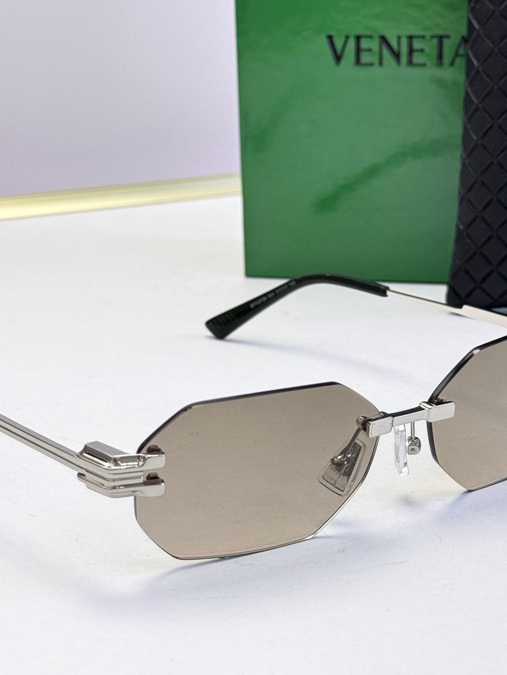 Bottega Veneta sunglasses close-up with silver frame and taupe tinted lenses, octagonal.