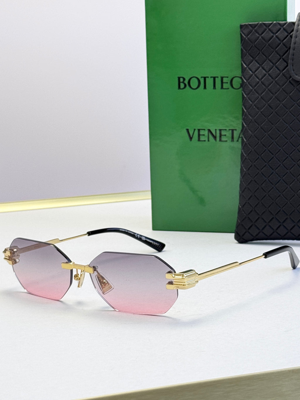 Bottega Veneta sunglasses with gold frame and pink tinted lenses, octagonal shape.