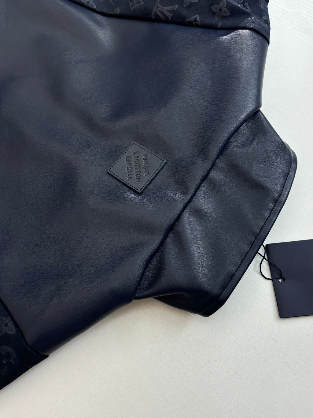 Navy jacket chest close-up with small gray logo patch and fabric sheen