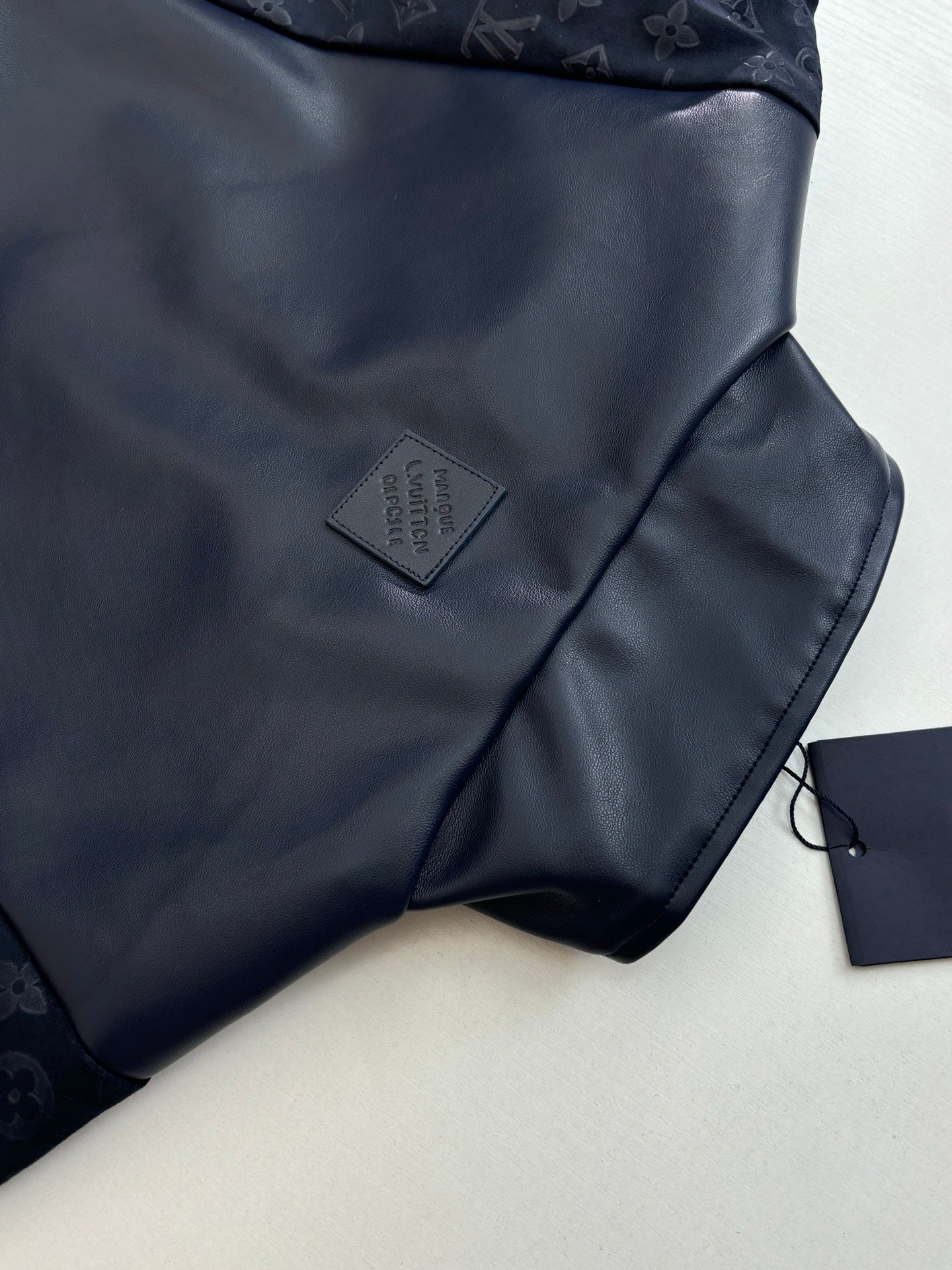 Navy jacket chest close-up with small gray logo patch and fabric sheen