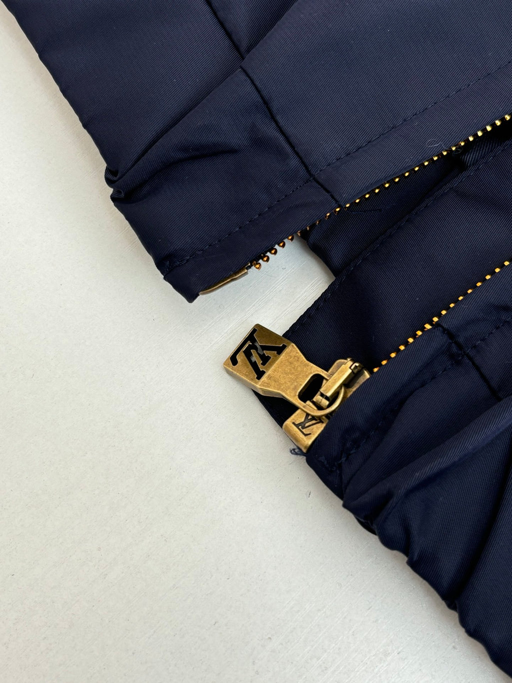 Navy pants leg close-up with gold zipper pull and LV-style belt logo hardware
