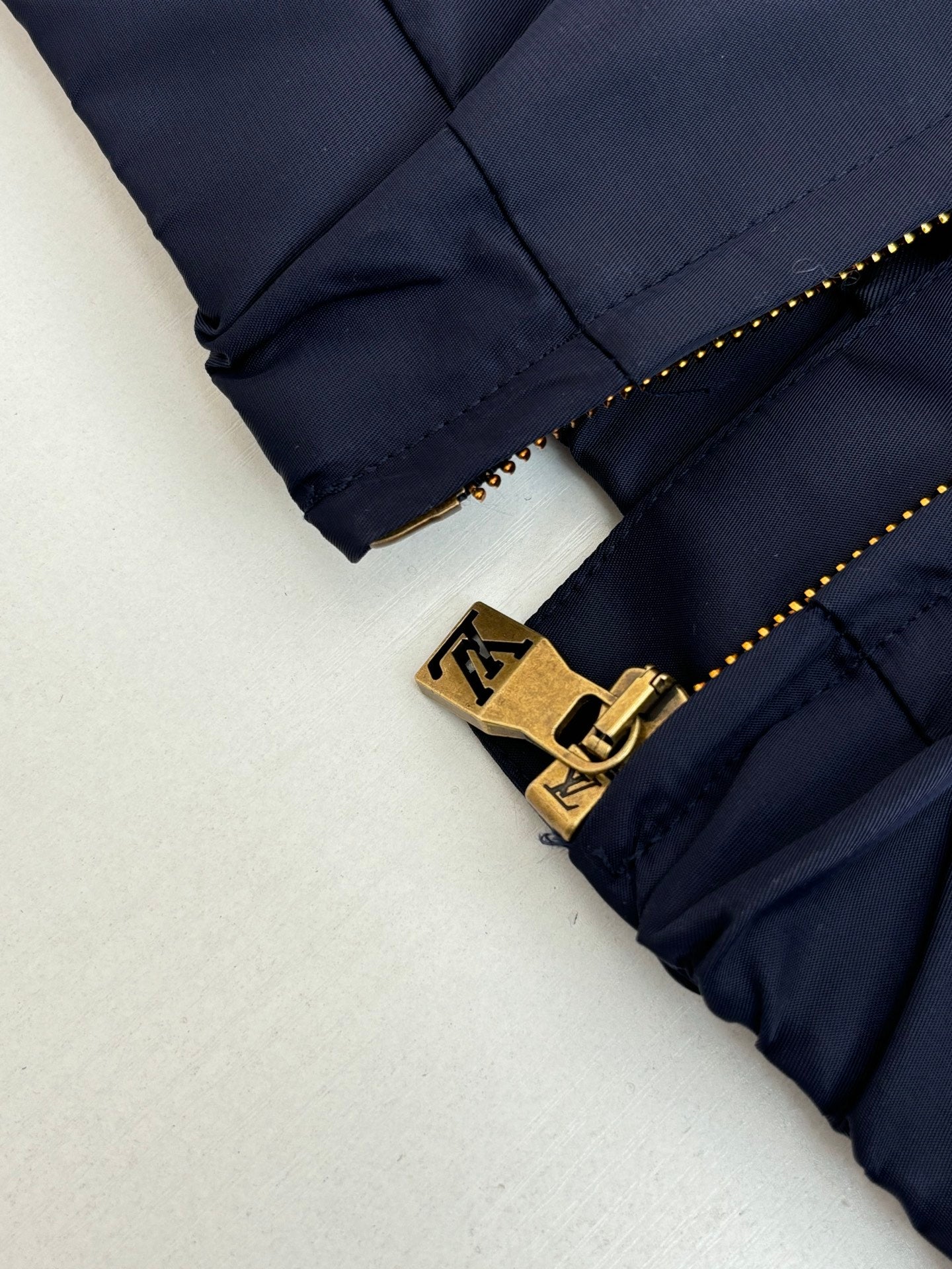 Navy pants leg close-up with gold zipper pull and LV-style belt logo hardware