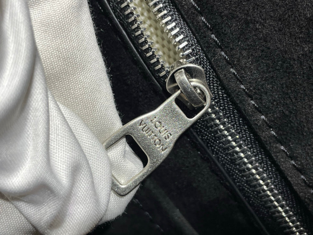 Metal zipper pull with logo tag on black bag, white cloth partly visible