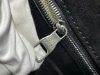 Metal zipper pull with logo tag on black bag, white cloth partly visible
