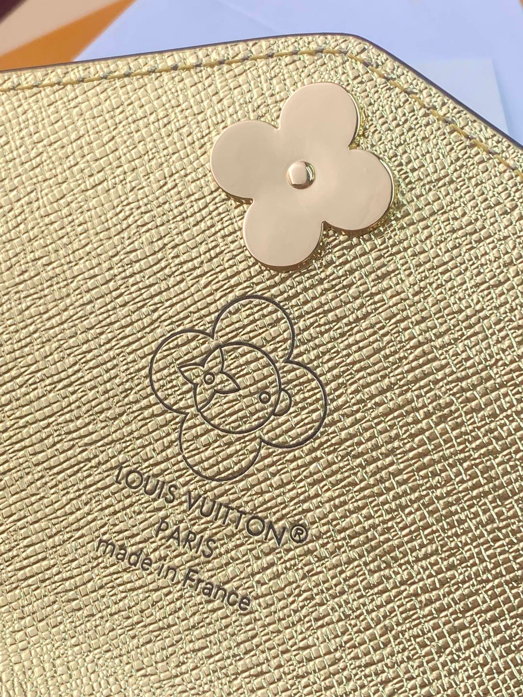 Louis Vuitton small bag close-up: gold textured flap with clover logo and embossed mark.