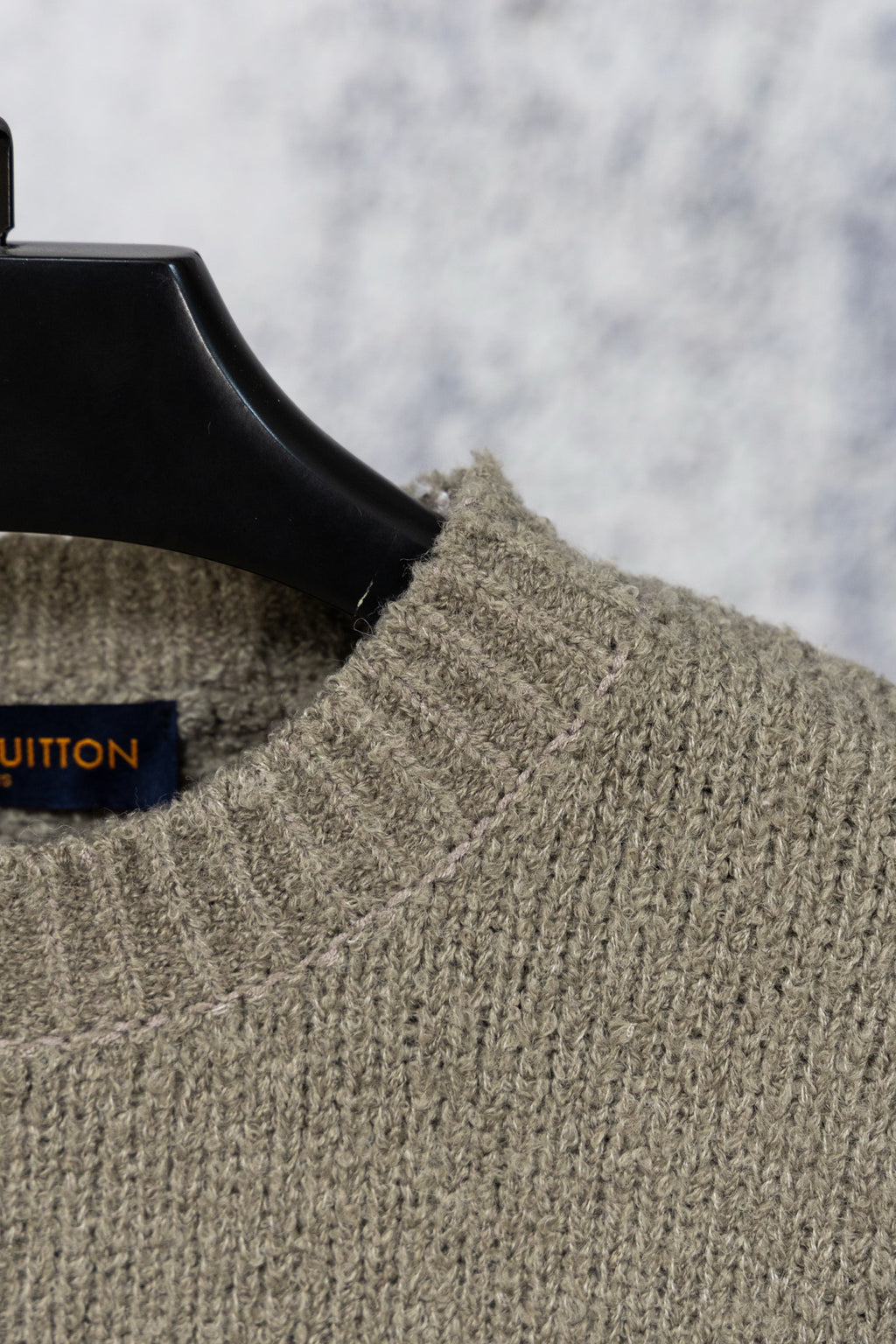 Khaki knit sweater collar with blue Louis Vuitton label on hanger