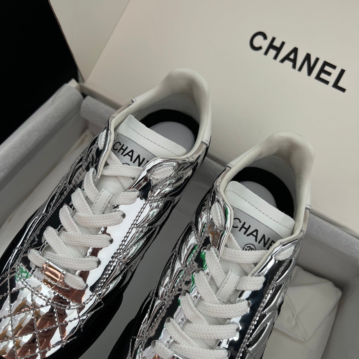 Metallic silver sneakers with white laces and green accent details