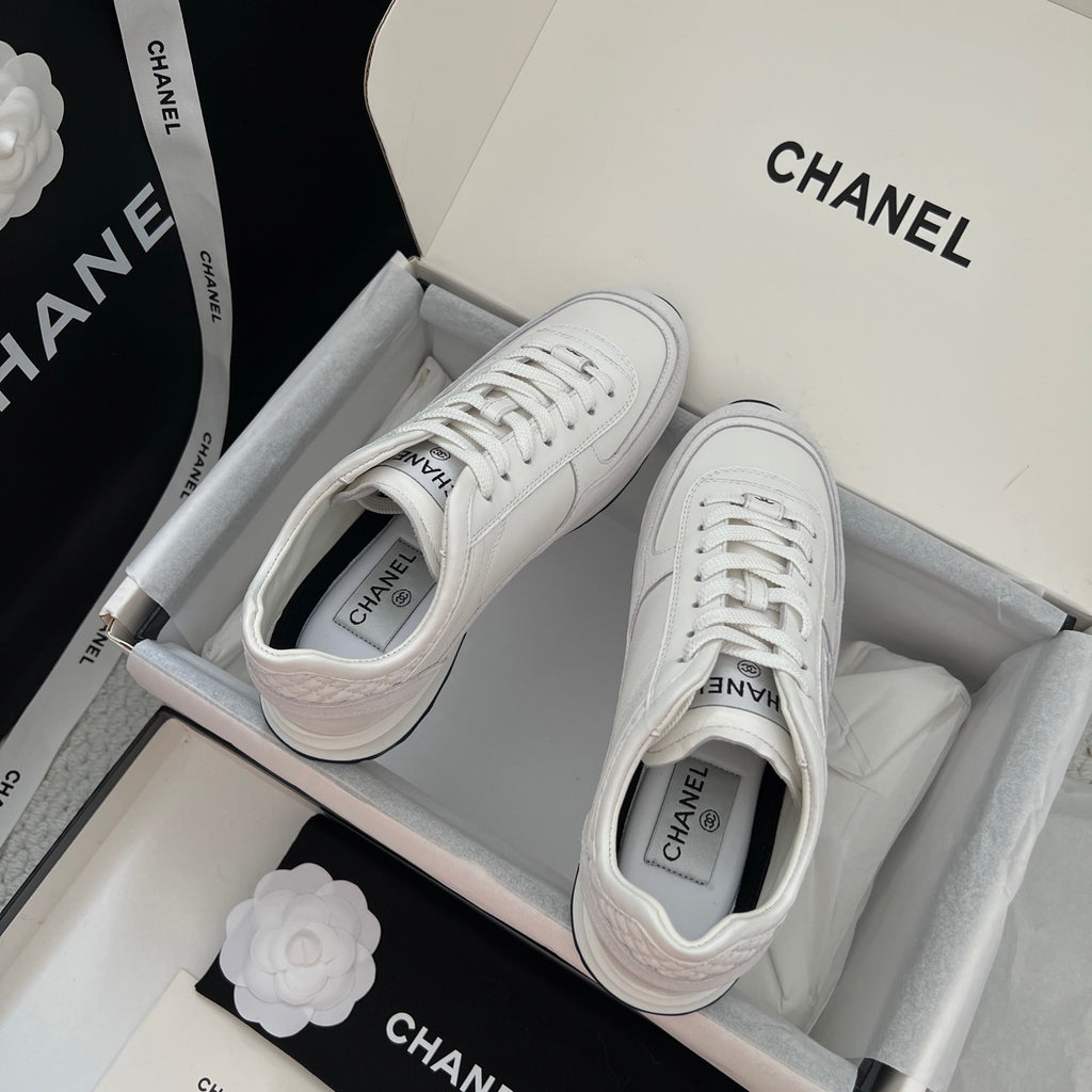 Pair of white Chanel unisex lace-up sneakers laid in a box.