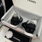 Back view of black Chanel unisex sneakers in box, white soles visible