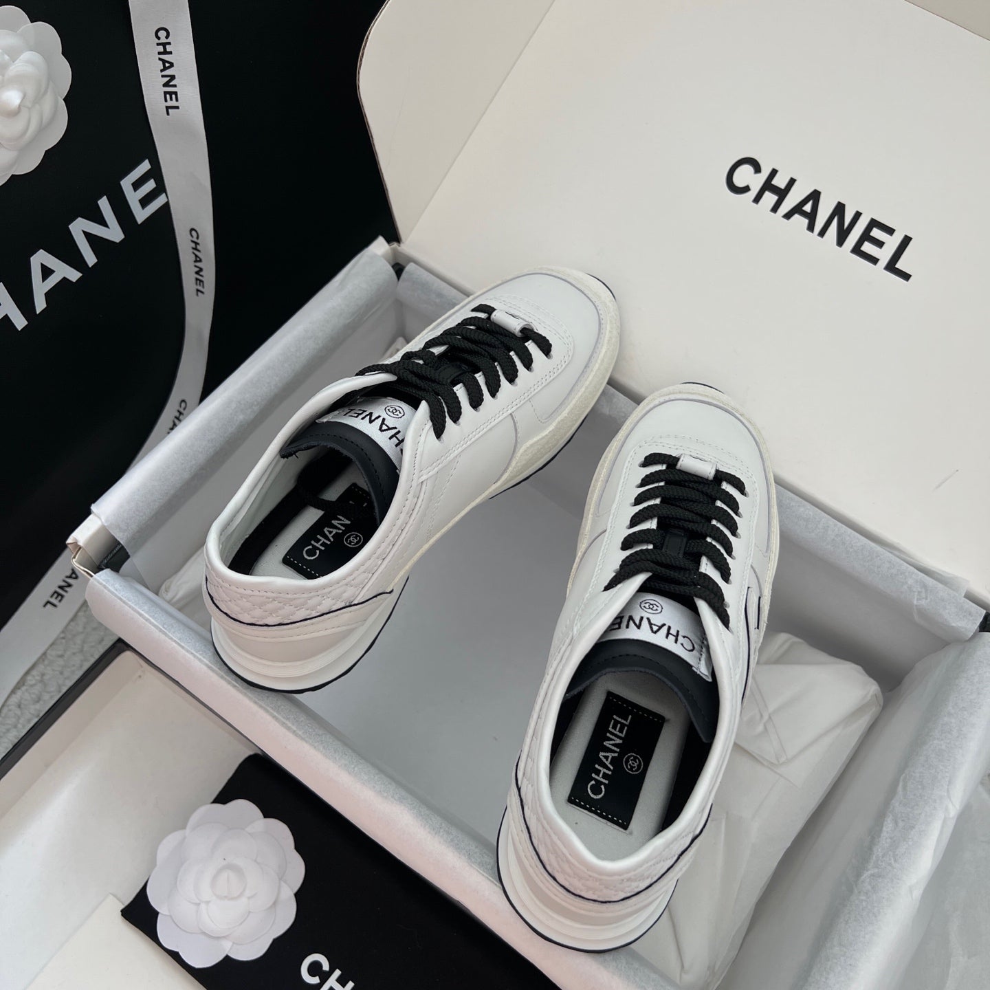 Pair of white leather sneakers with black laces and Chanel logo on insoles