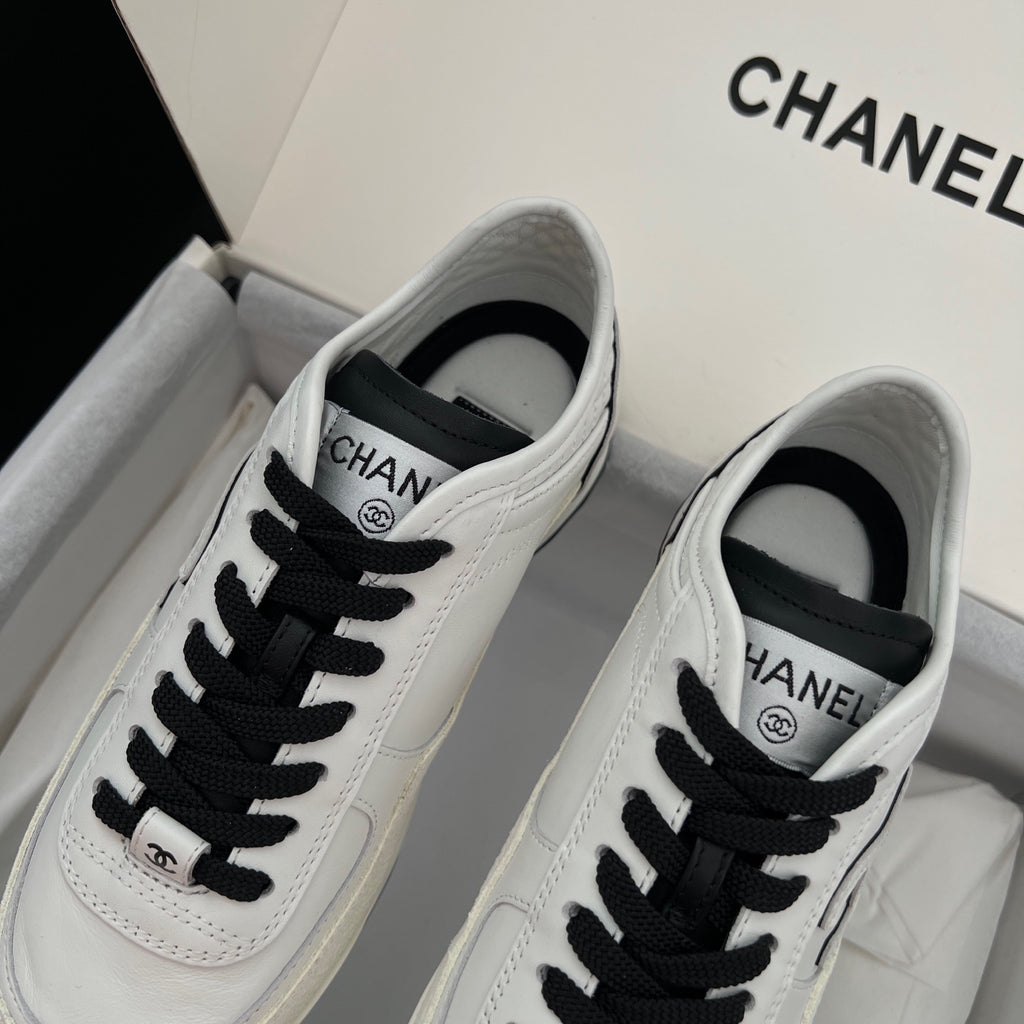White leather low-top sneakers with black lace-up and Chanel logo patch