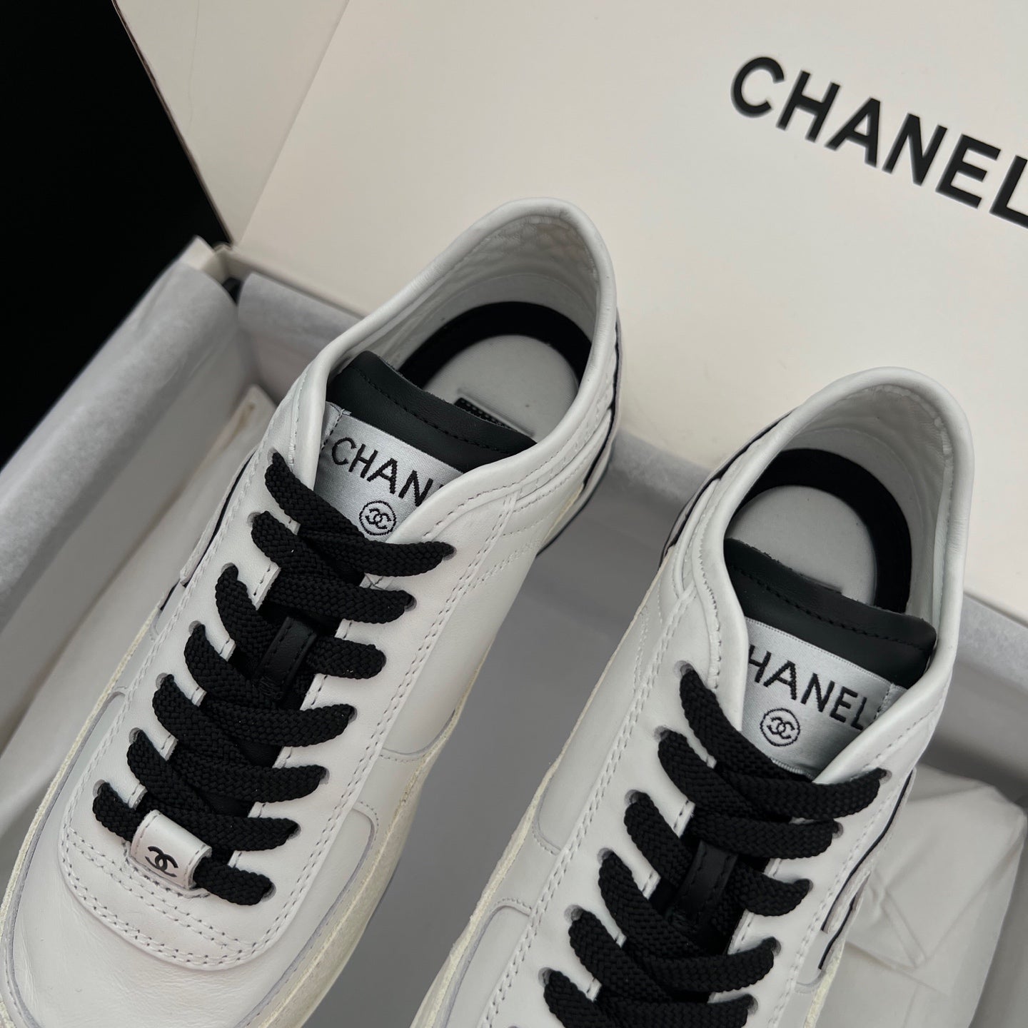 White leather low-top sneakers with black lace-up and Chanel logo patch