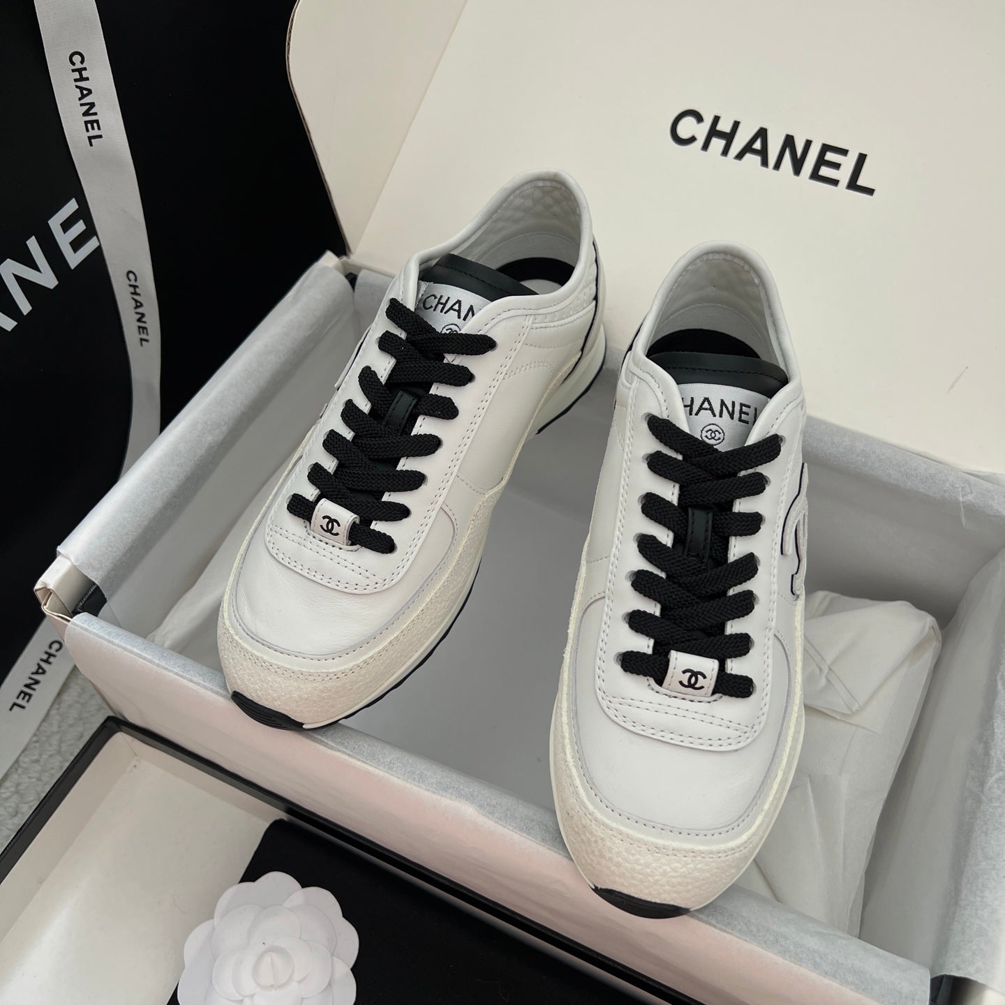 White leather sneakers with black laces and Chanel logo on tongue