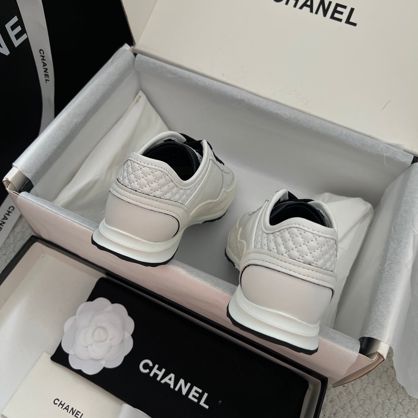 White leather sneakers with black laces, heel view with Chanel logo accents